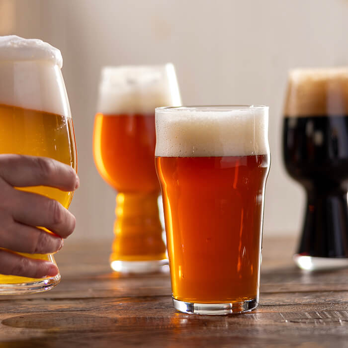 a hand placing a glass of beer on a table holding several other beers of various colors